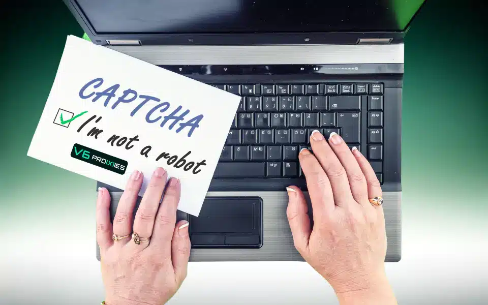 a pair of hands interacting with a laptop computer on a desk. The laptop is open, displaying a visible keyboard. One hand is holding a white paper sign with handwritten text that reads "CAPTCHA" along with a checkbox next to the phrase "I'm not a robot," which is checked. The paper also carries the logo "V6 Proxies".